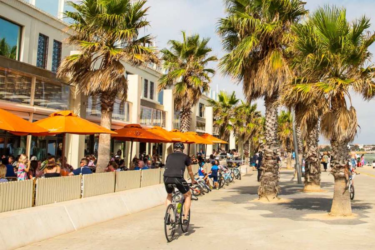 A bike rider cycling past the beach and restaurants in St Kilda 