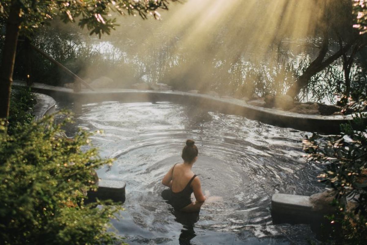 young woman bathing in hot springs surrounded by trees and sunlight