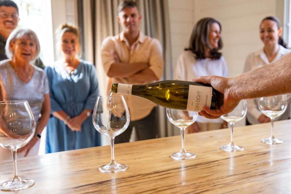 six guests watch a man pour wine