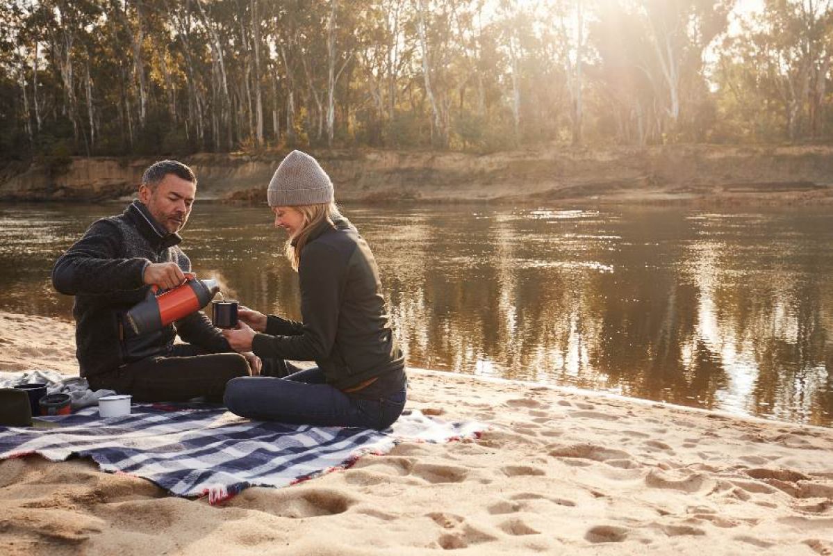 A man and a woman sitting on a picnic rug on a beach by the Murray River