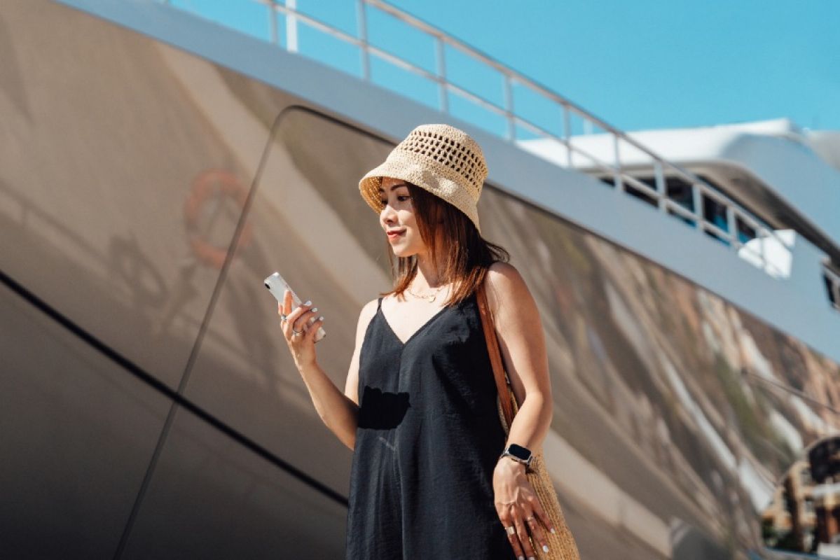 woman smiling at her smartphone as she stands in front of a cruise ship