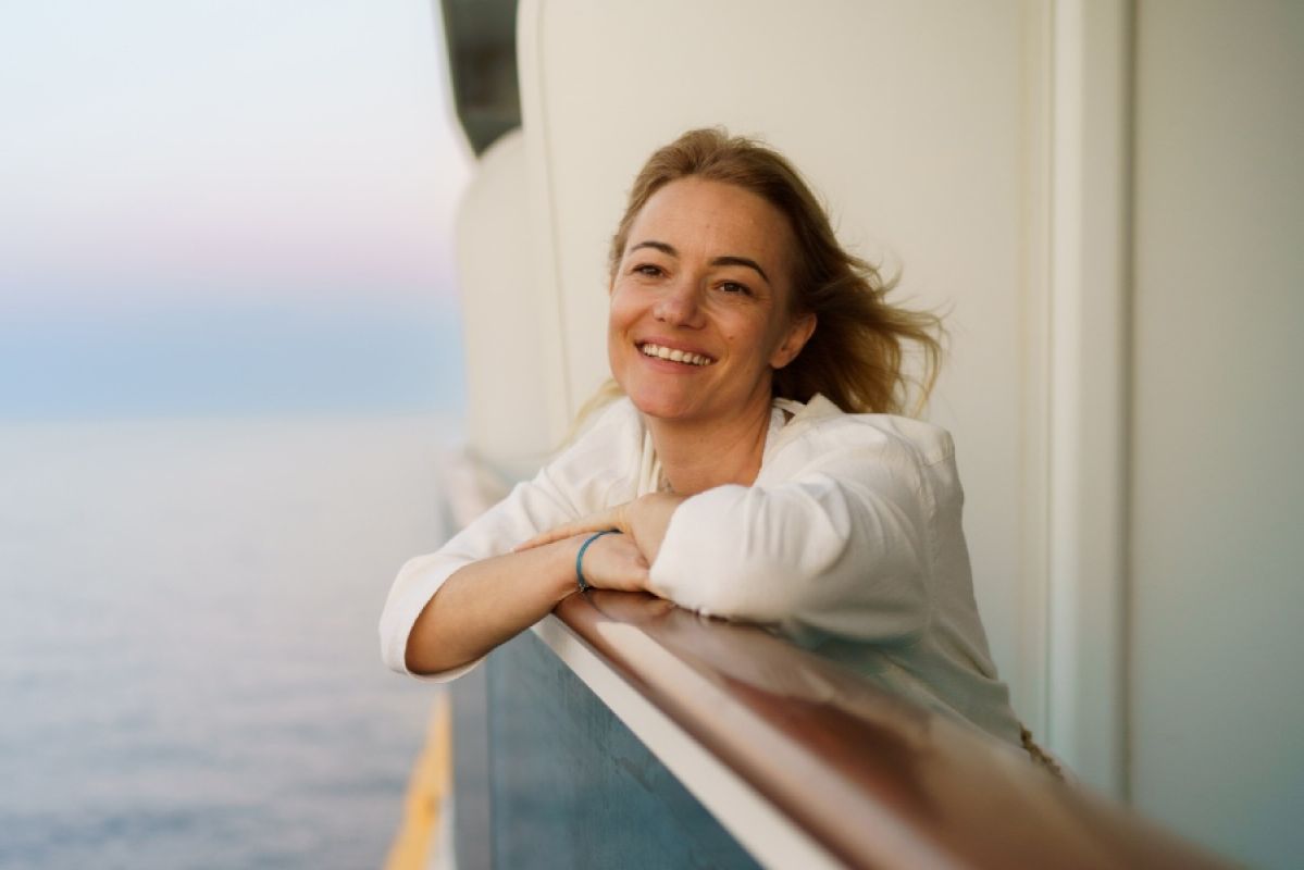 woman leaning on railing of cruise ship smiling