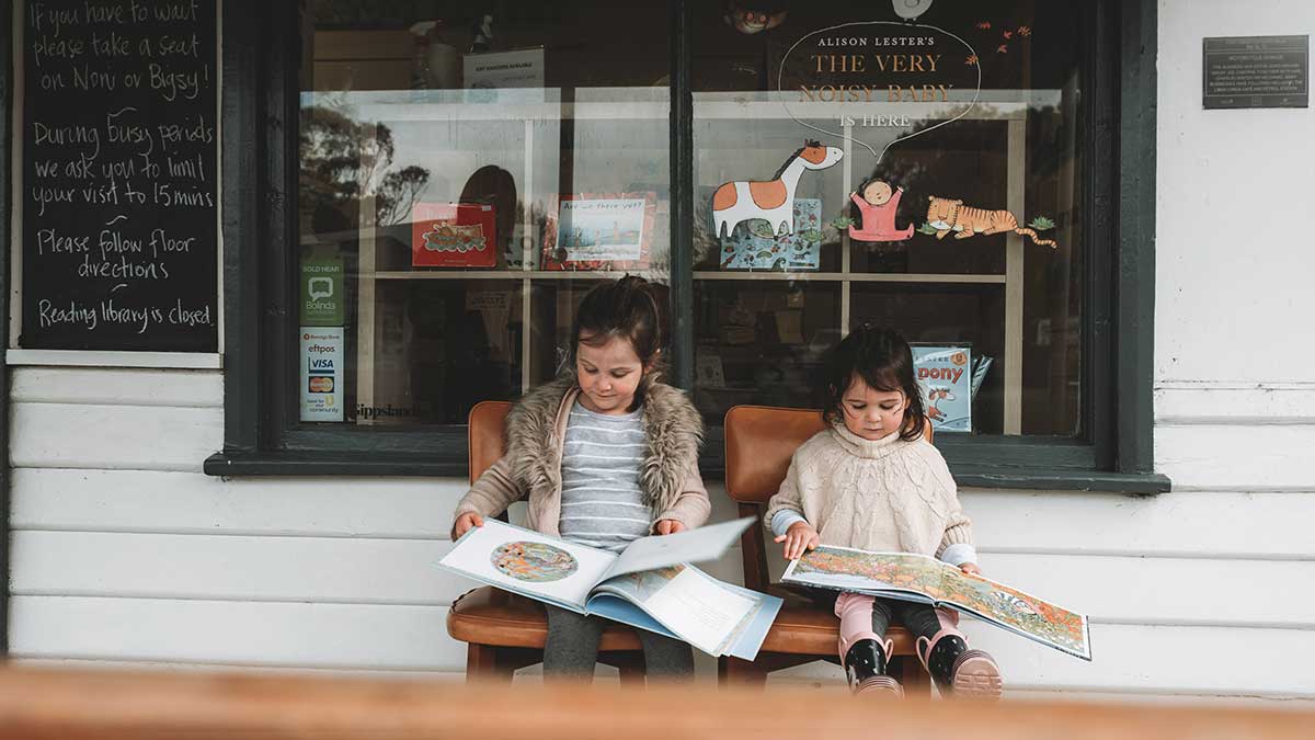 two children reading books outside a shop