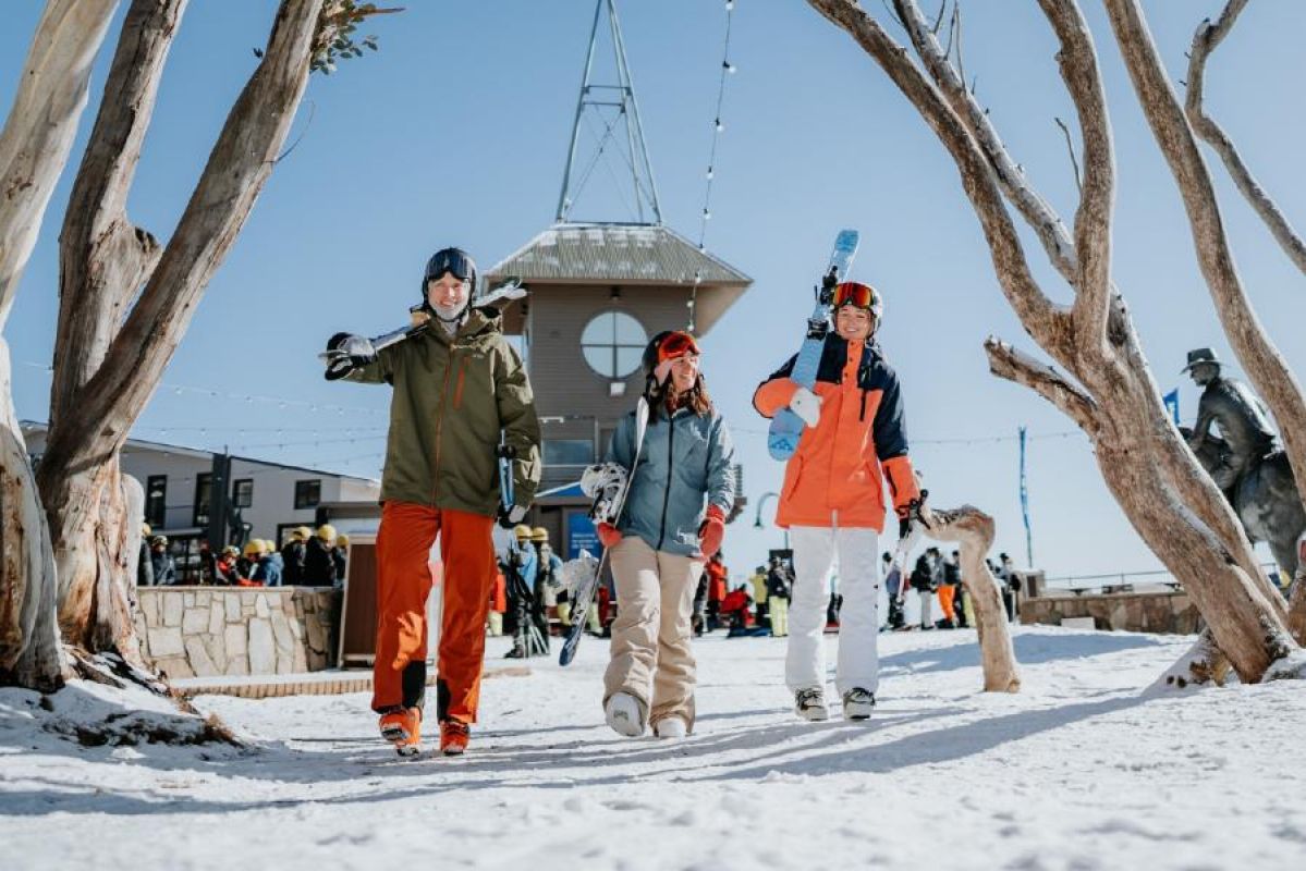 three friends dressed in snow gear carrying skis at Mt Buller, Victoria