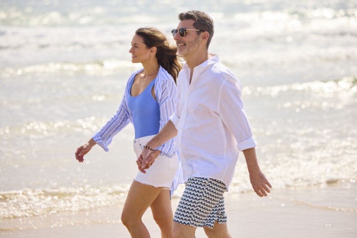 woman and man holding hands and smiling as they walk down a beach