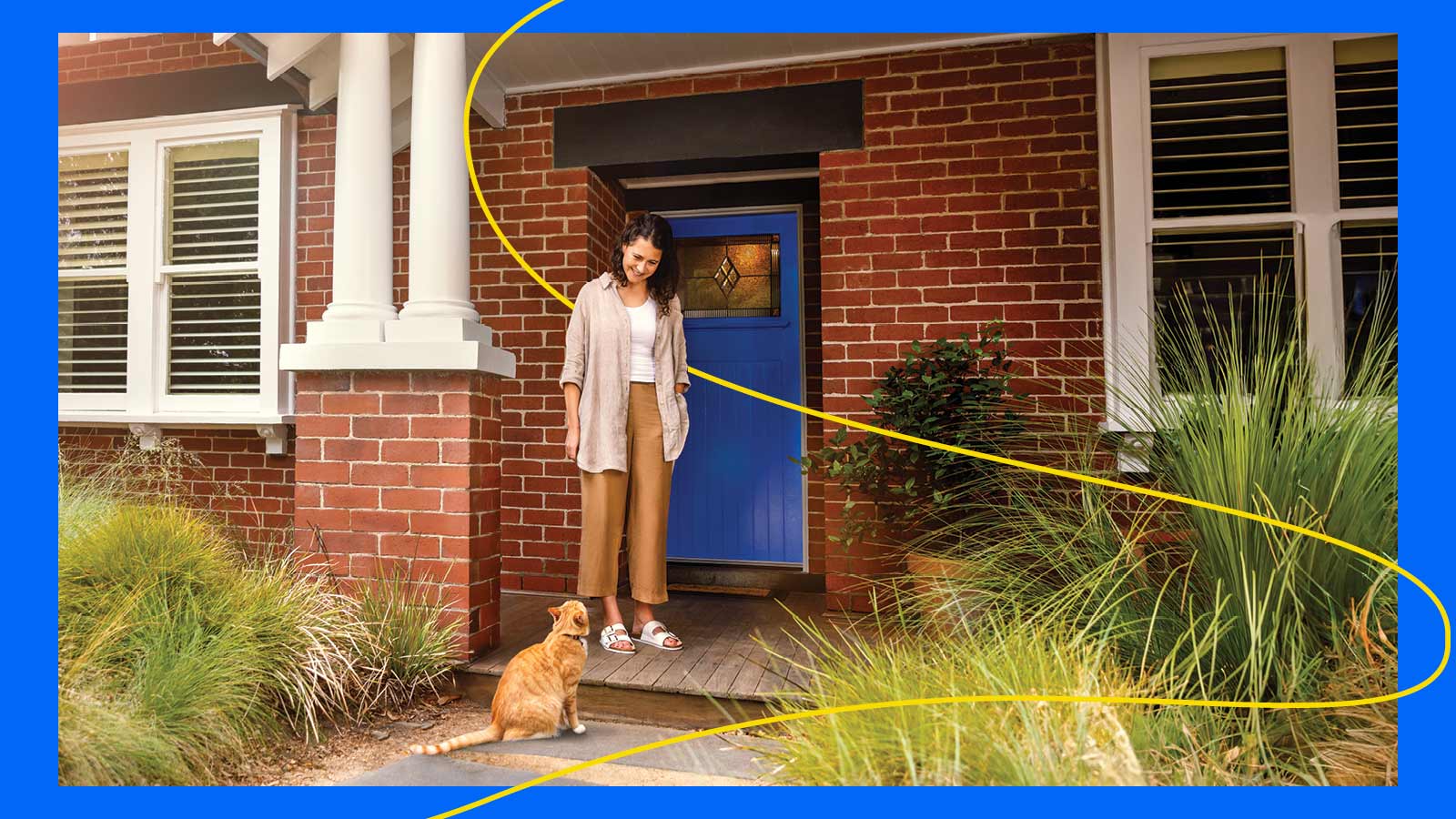 Woman in front of a blue door smiling down at an orange cat.