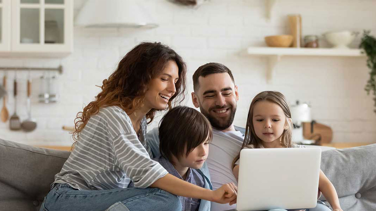 Parents and two children sitting on a grey couch, looking at a laptop and smiling. 