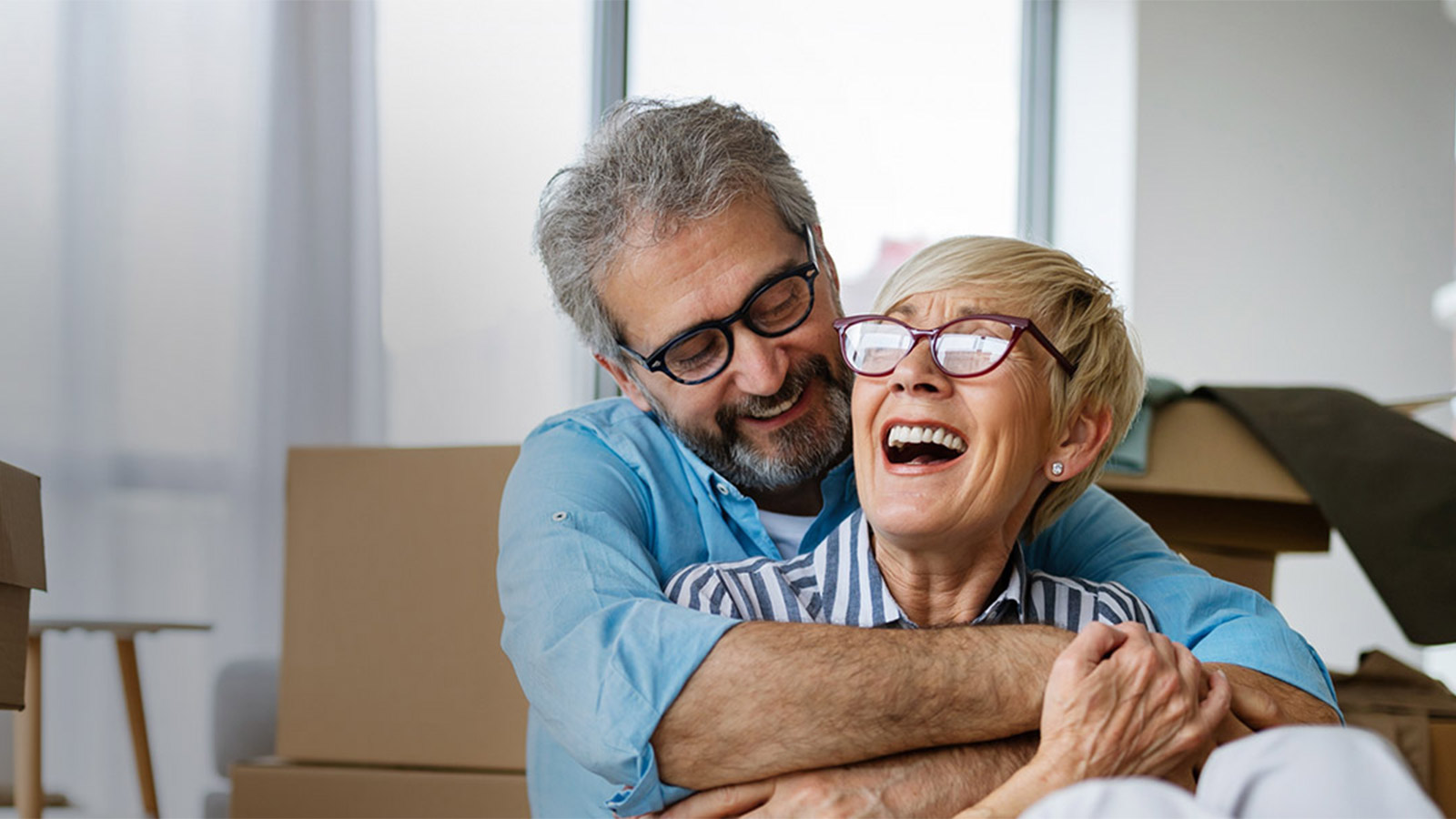 Happy middle aged couple sitting on the floor, surrounded by moving boxes, and laughing.