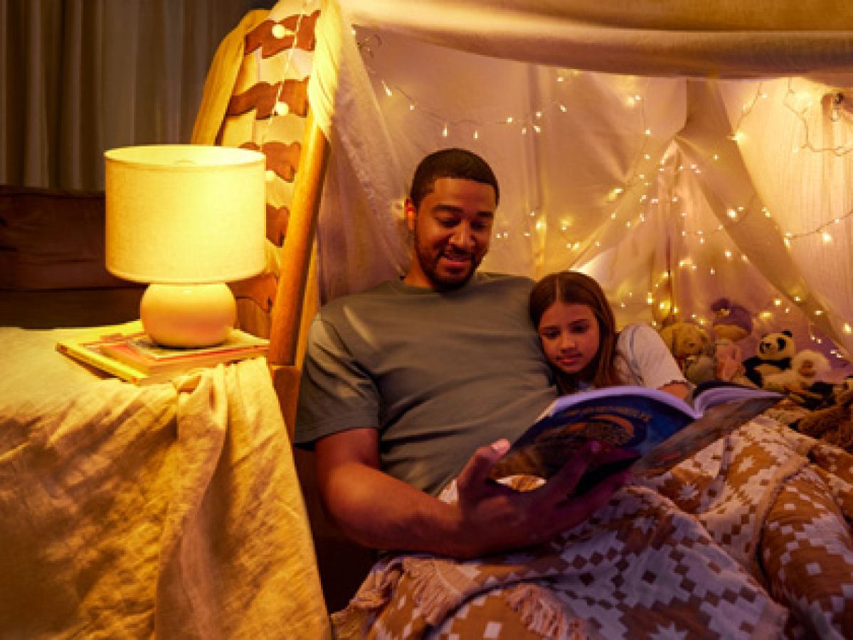Father and daughter reading a book under some fairy lights.
