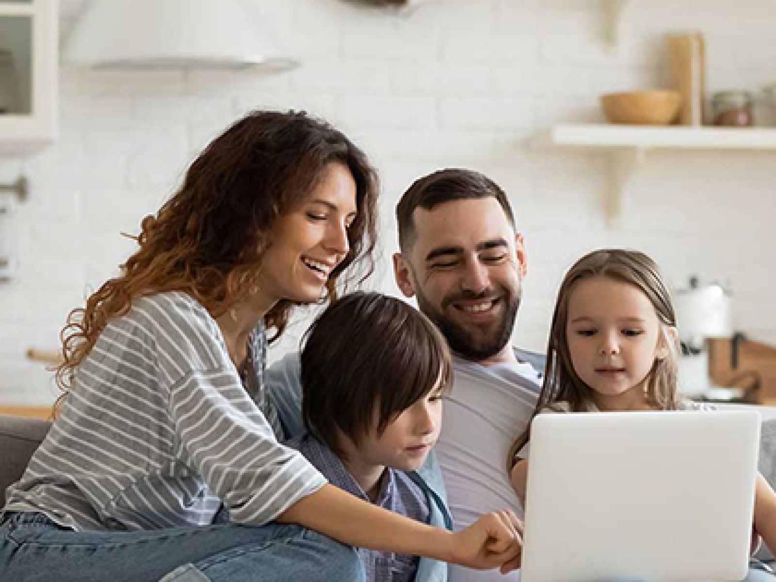 Parents and two children sitting on a grey couch, looking at a laptop and smiling. 