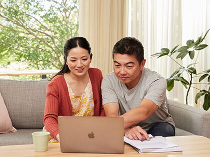 A woman and a man sit on the couch looking at their laptop.