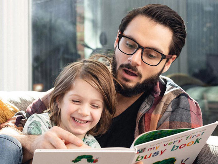 father and son reading book on couch