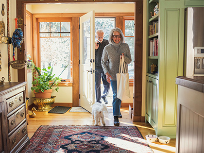 Couple walking into their home, being greeted by their dog.