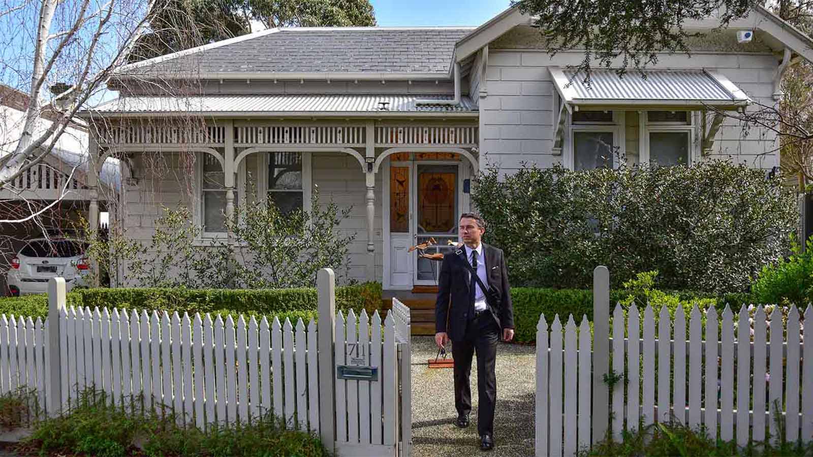 Man in a suit leaving his weatherboard house.