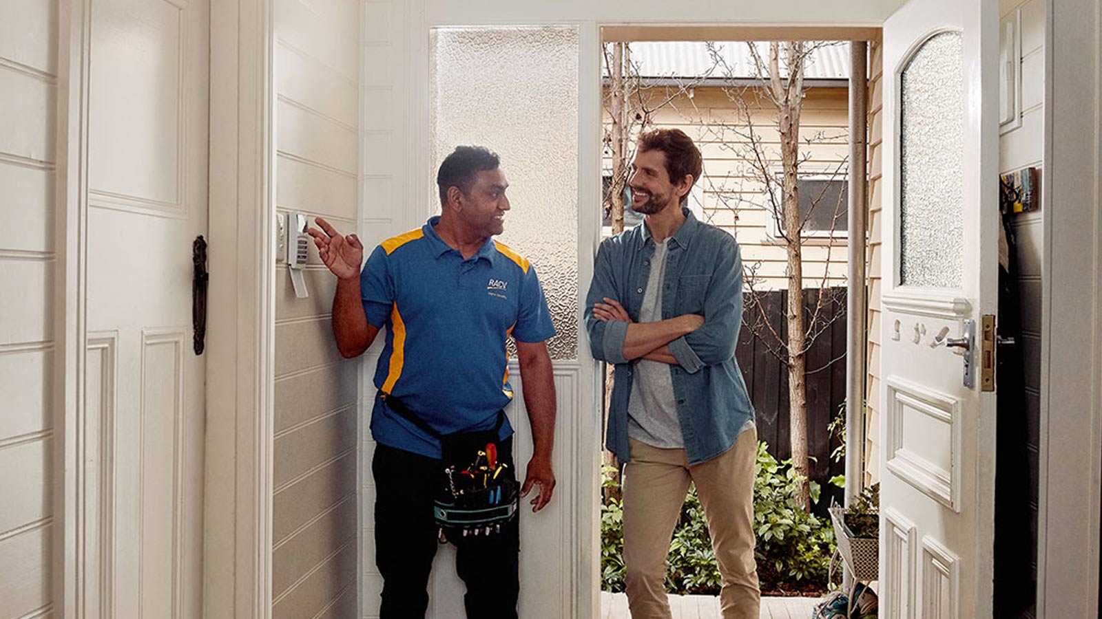 RACV Tradesman chatting to a member inside their house, whilst pointing at an alarm system.