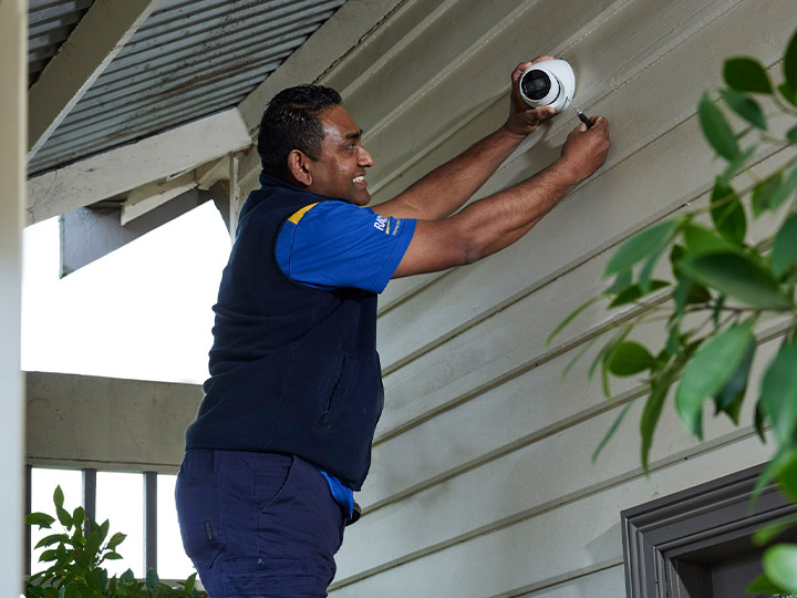 RACV Tradesman smiling and holding a screwdriver, while installing a camera.