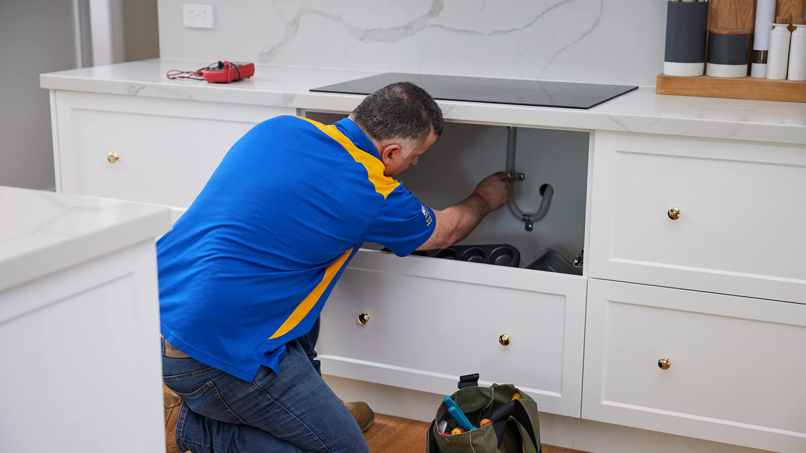RACV tradesperson installing induction cooktop.