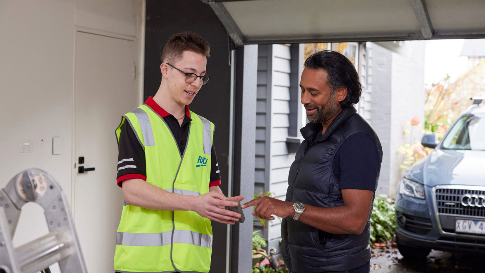 Tradesman showing garage door remote to smiling homeowner whilst standing inside of the garage.