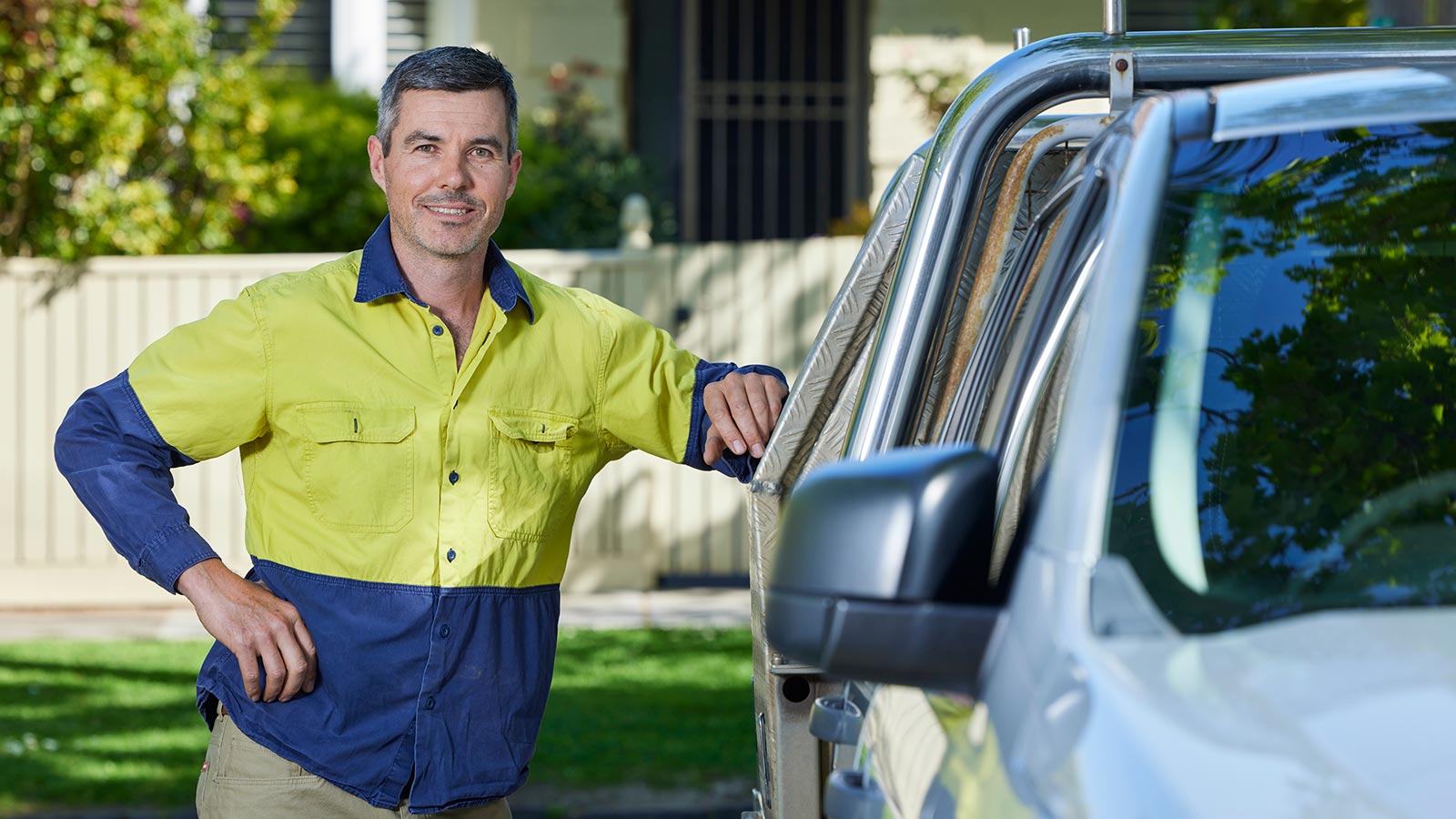 Plumber in work clothes leaning against their work ute