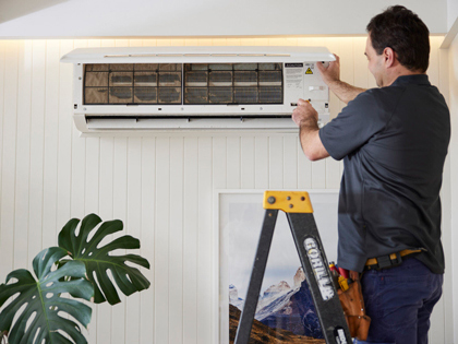 Tradesman standing on a ladder, opening an air conditioning unit and pressing a button.