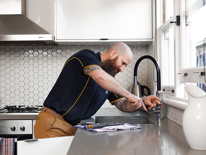RACV plumber working on a kitchen tap.