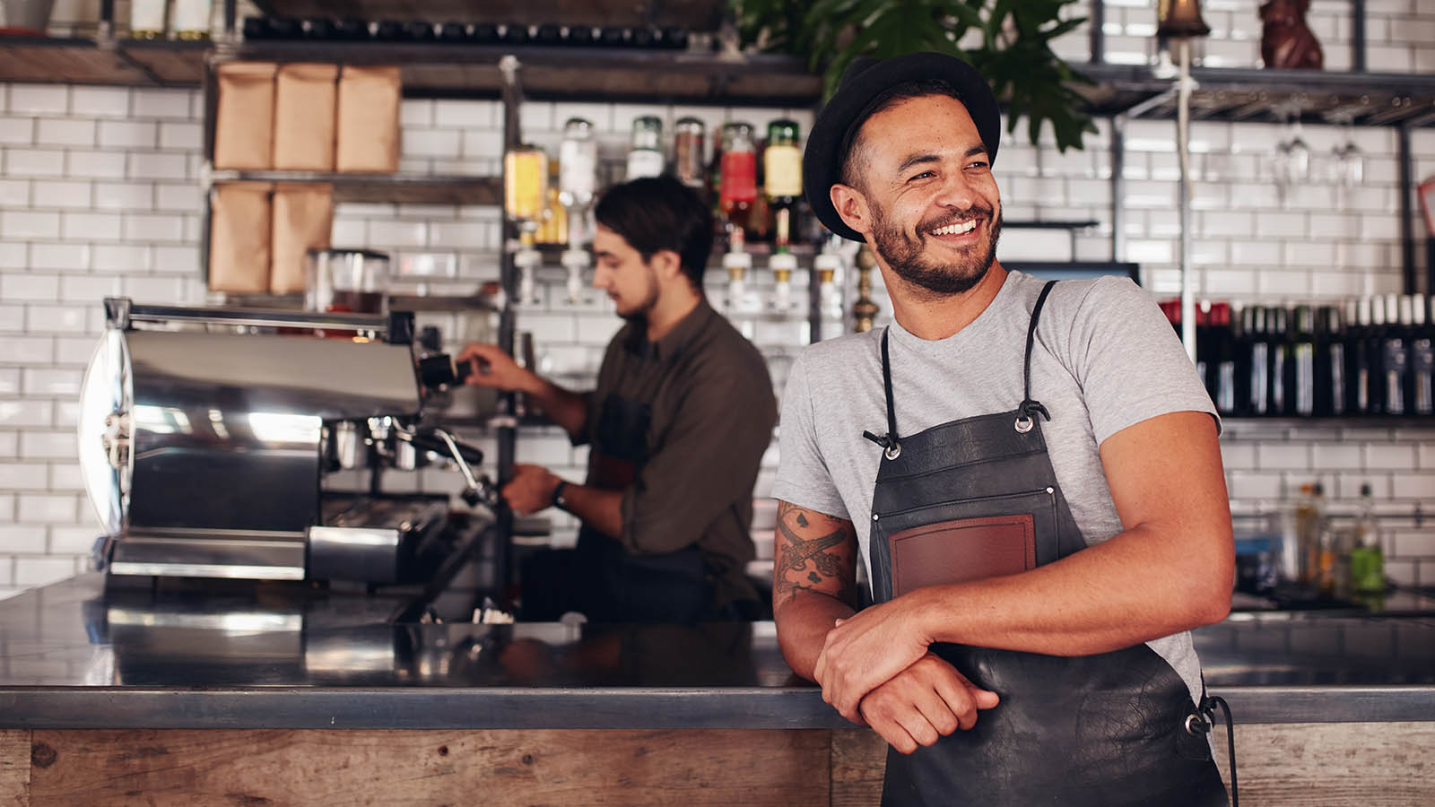 Barista in a stylish cafe making coffee and man standing in front of the counter smiling.