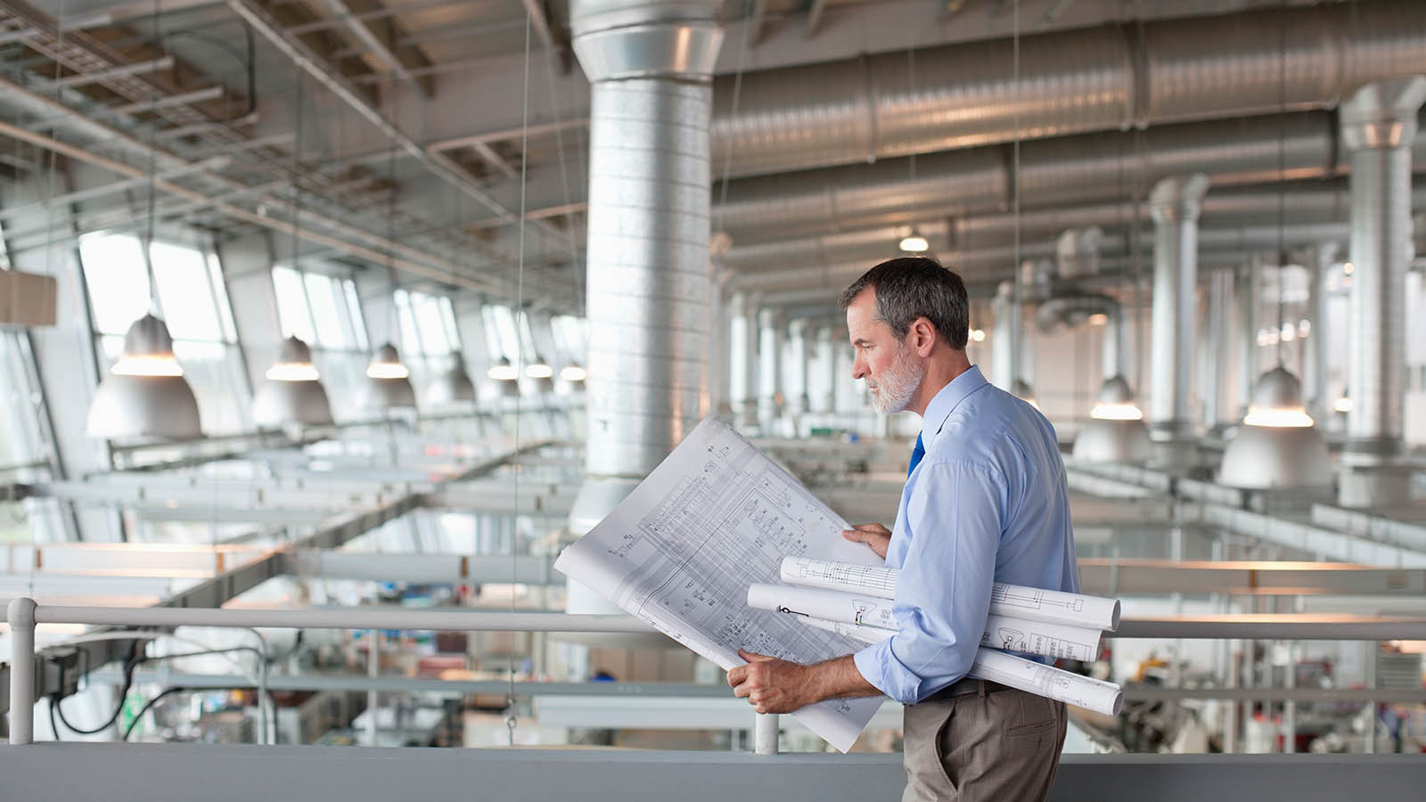 Man walking across a mezzanine in a commercial property holding blueprint plans.