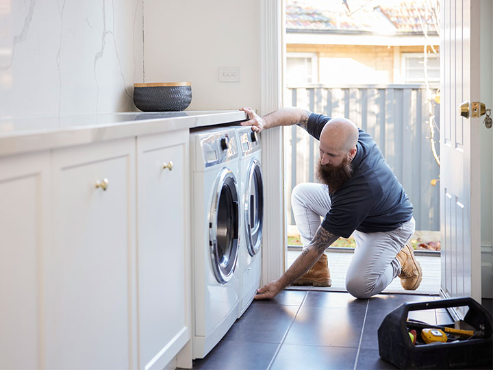 Tradesperson kneals to fix washing machine at a customer's house.