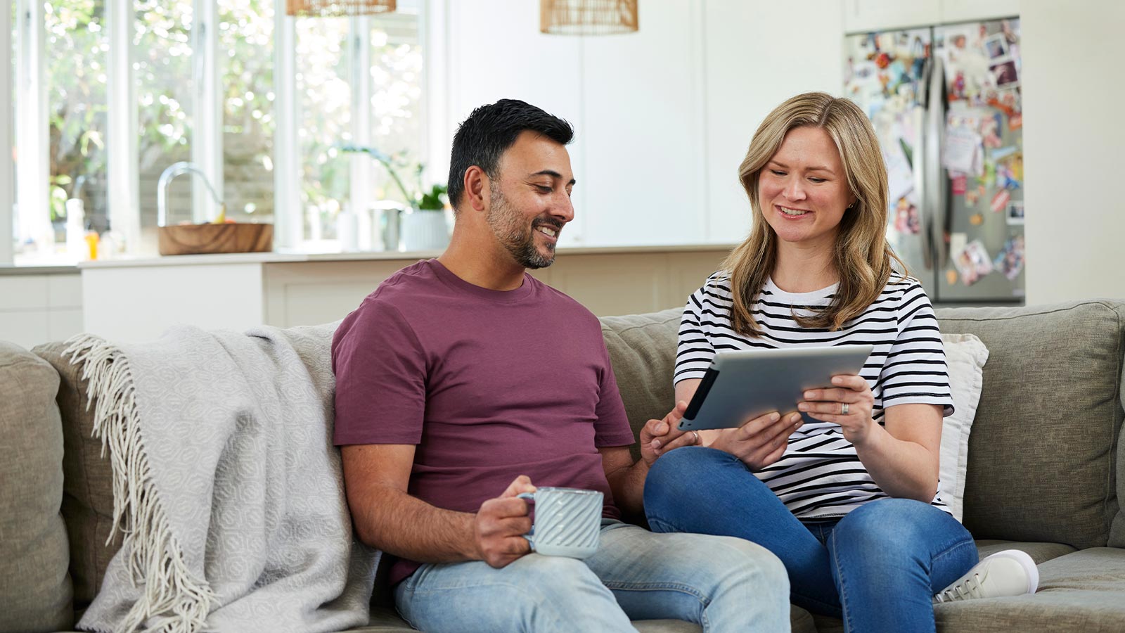 Couple sitting on their couch while smiling and looking at their iPad.