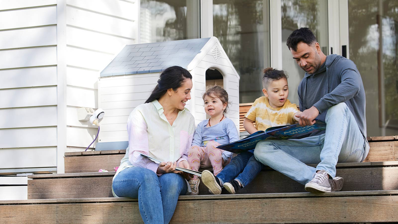 Family reading books together, while sitting on their outdoor deck stairs.