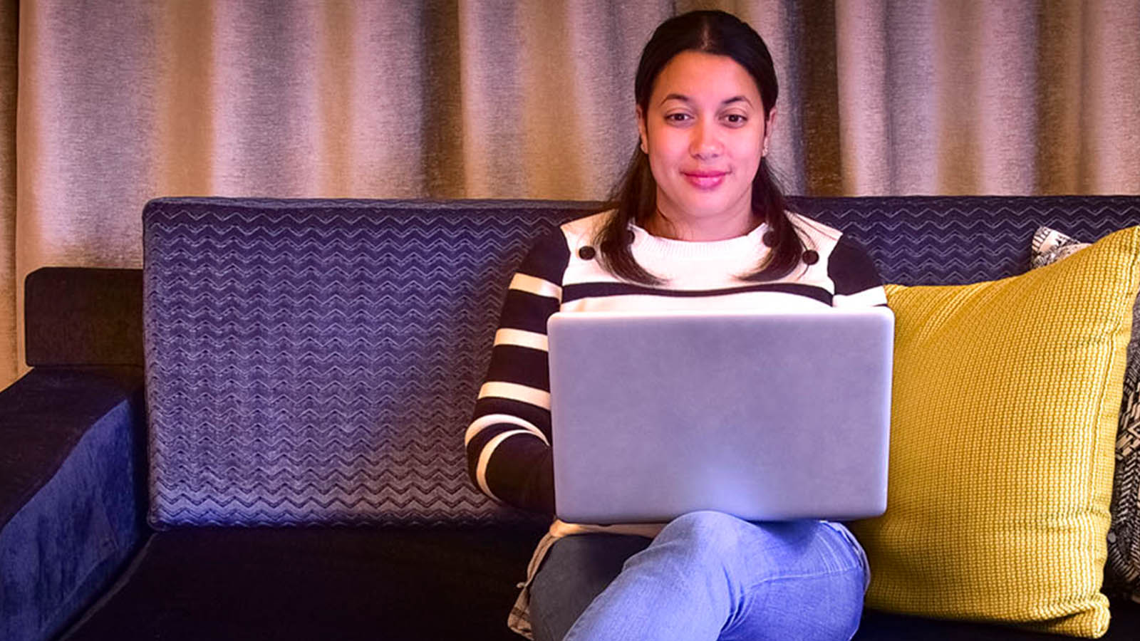 Woman with a laptop sitting on a lounge with colourful cushions