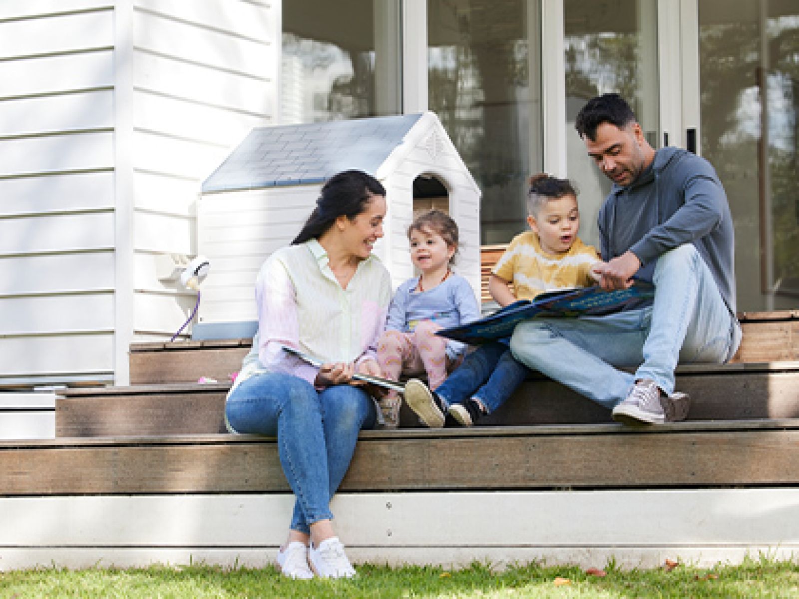 Family reading books together, while sitting on their outdoor deck stairs.