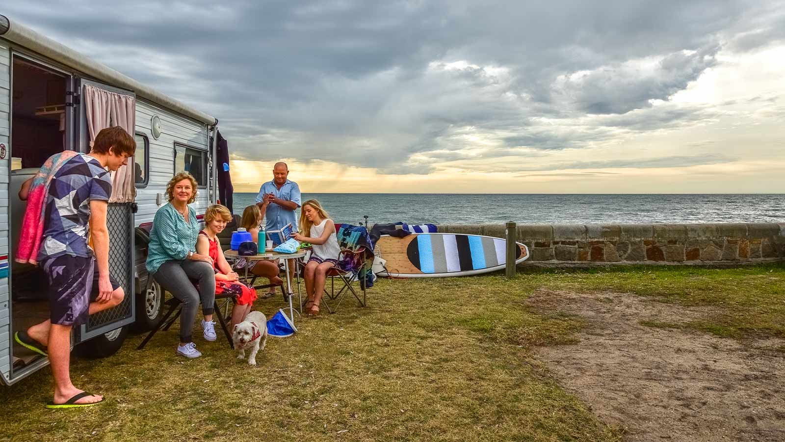 A family sitting together outside their caravan, overlooking the ocean.