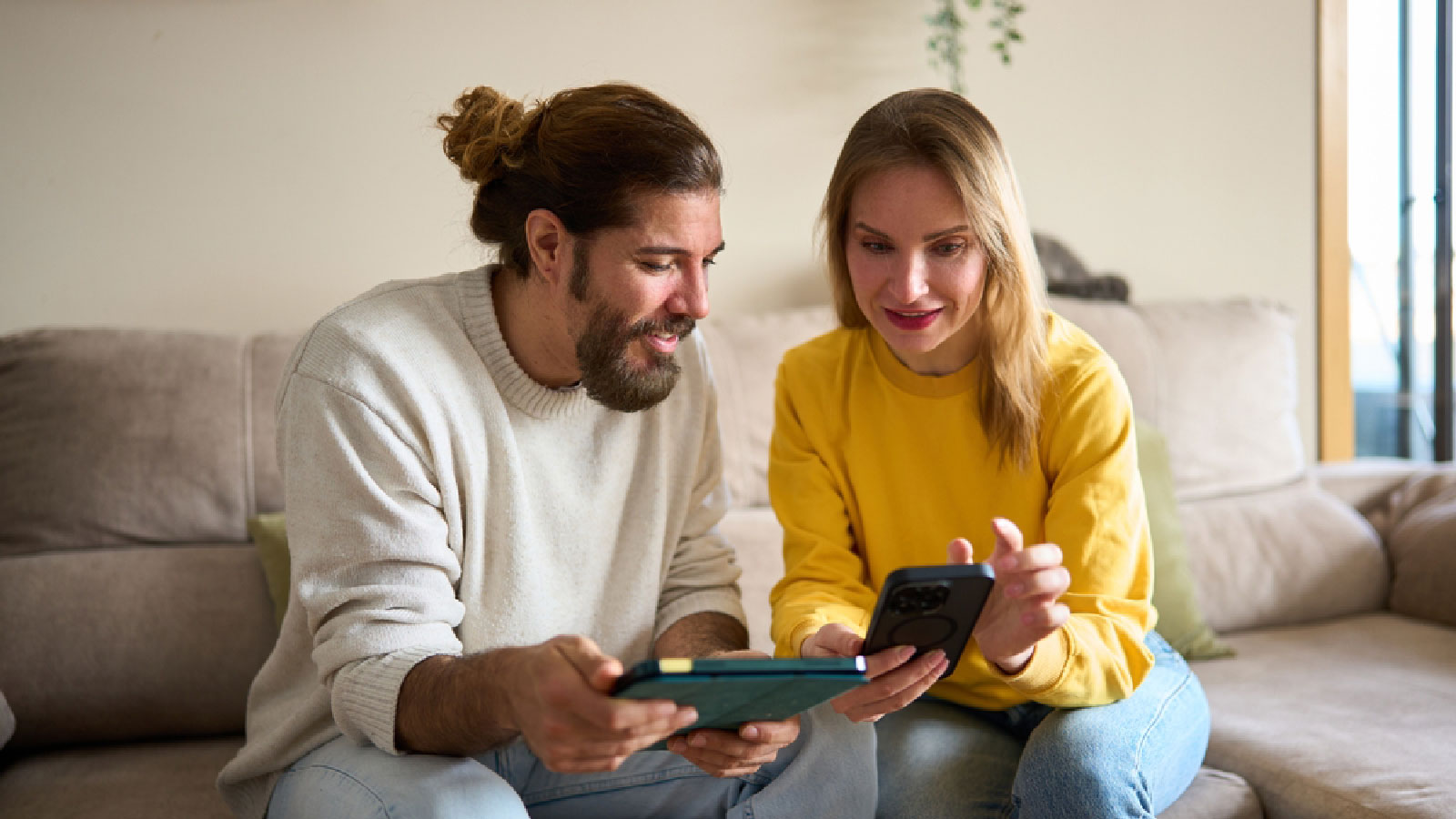 A couple comparing something using their phone and tablet devices.