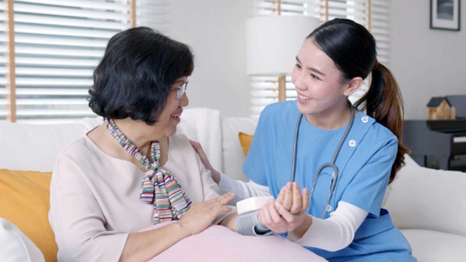Nurse wearing a mask and scrubs talking to an elderly woman.