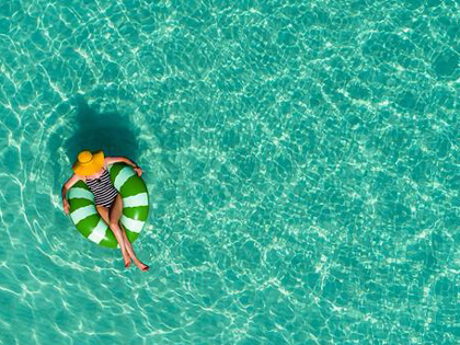 Woman wearing a sun hat in the pool, floating in a green inflatable pool donut.