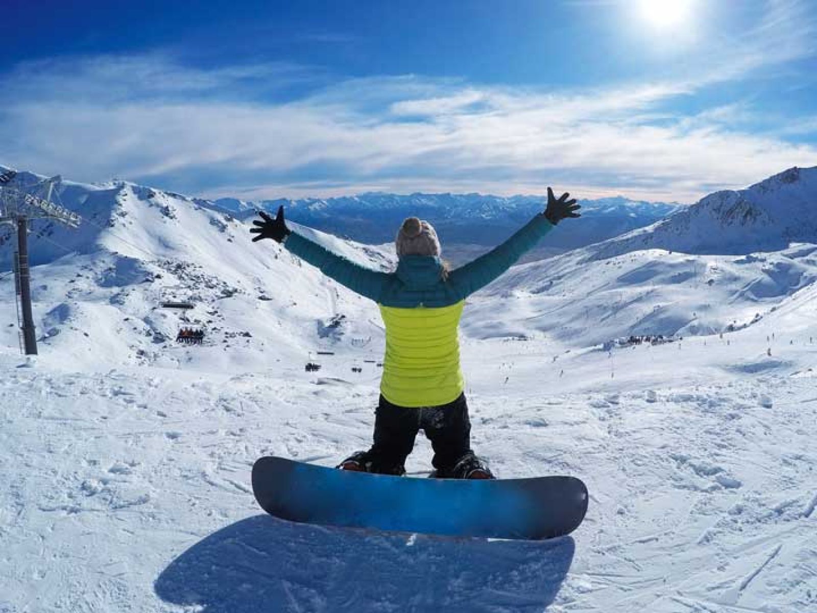 Woman with a snowboard on a mountain in the snow with her arms spread open to the view. 