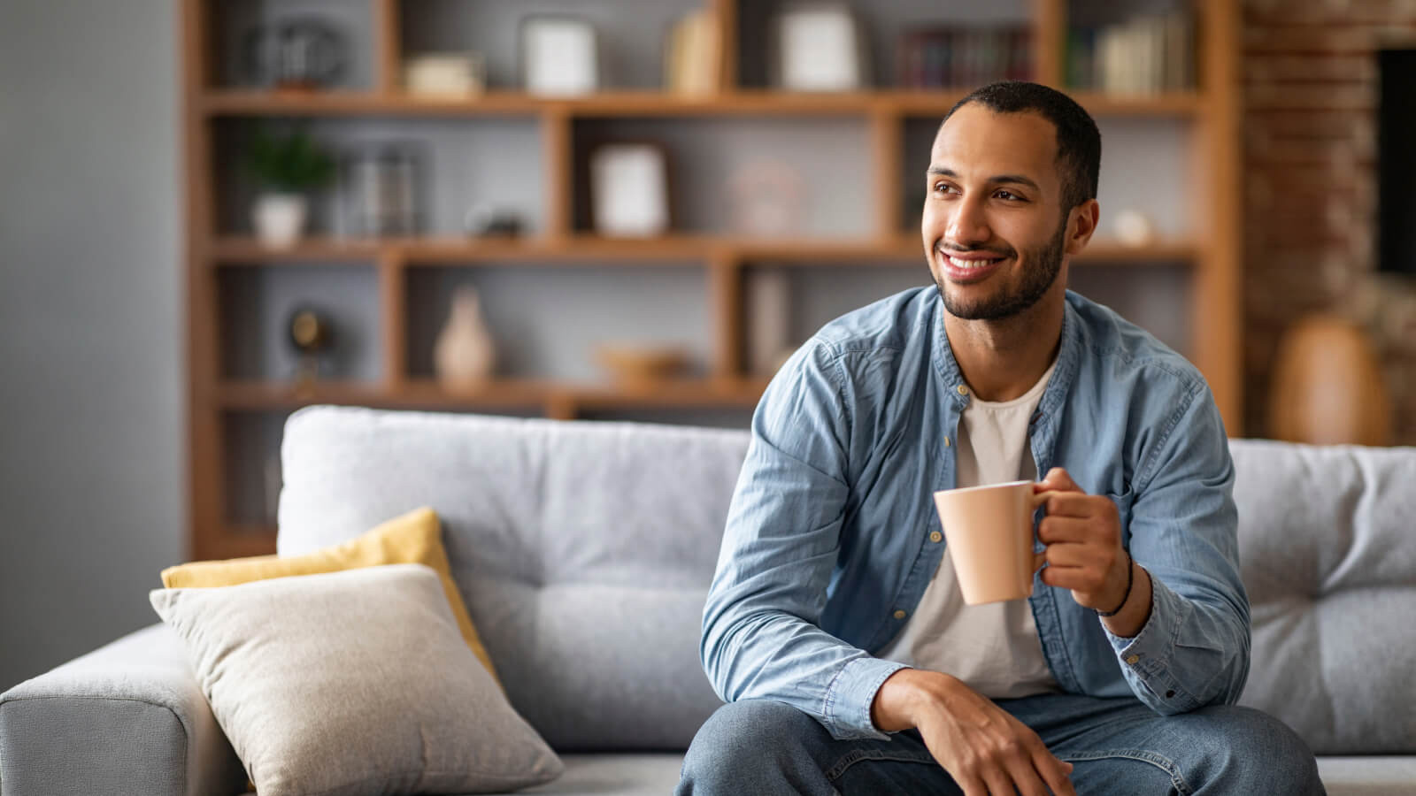 A man smiling andenjoying a cup o cofee whilst sitting on his couch. 