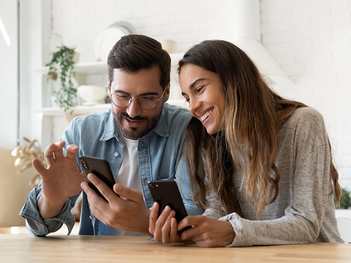 A couple smiling together while looking at their phones.