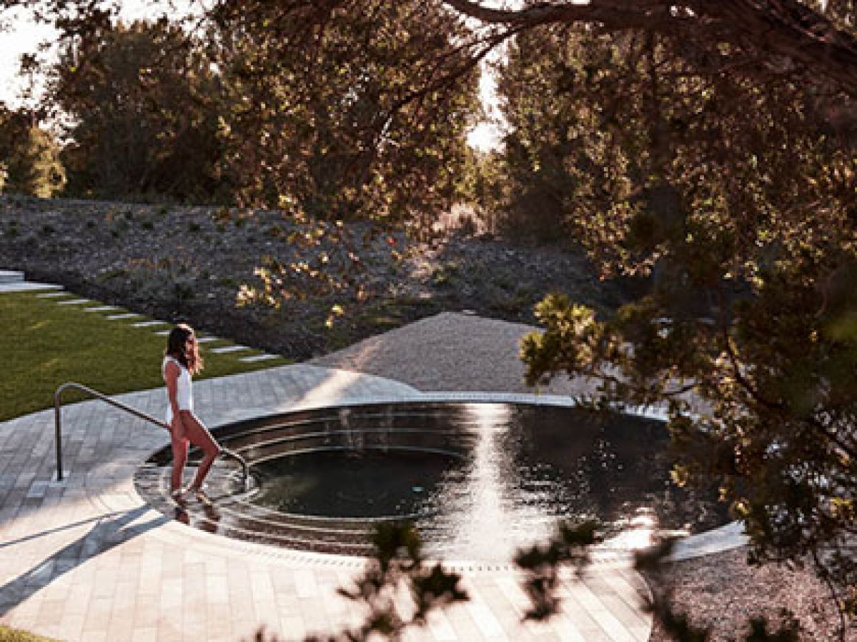 Woman walking into an outdoor spa surrounded by trees