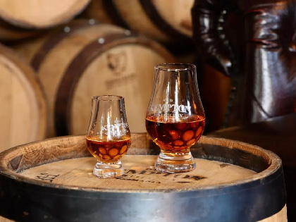 Two glasses of whiskey sitting ona  whiskey barrell