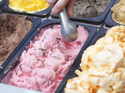 A hand scooping ice cream from a choice of several tubs of flavours. 
