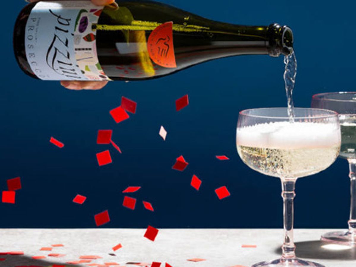 Champagne bottle filling a glass with confetti falling around it.