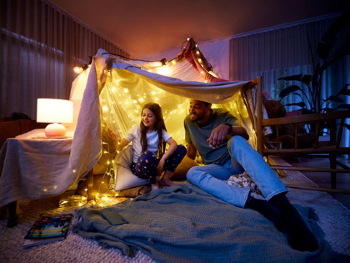 Dad and daughter smiling in a home built forte with fairy lights. 