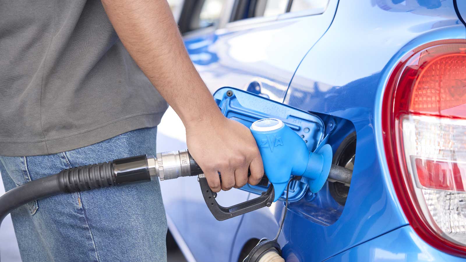 A man filling his blue car with fuel. 