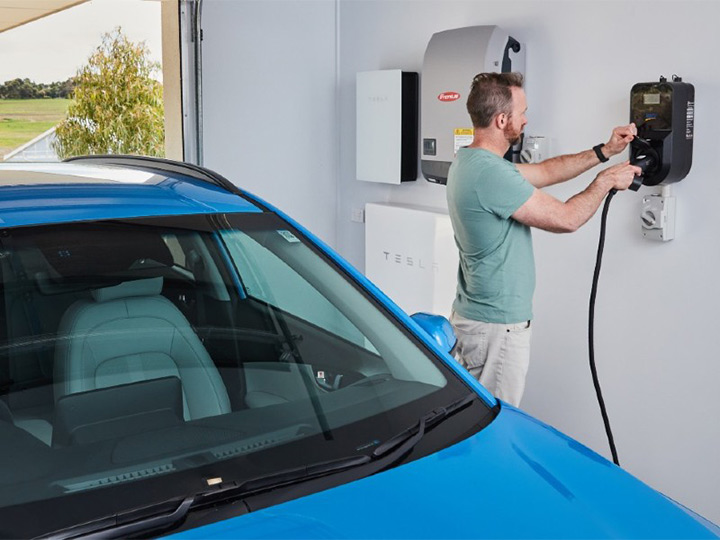 Electric vehicle owner connecting his blue car to a wall home charger.