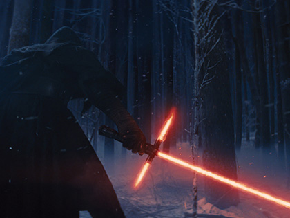 A hooded figure in a dark snow covered forest holding a red lightsaber.