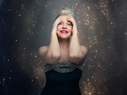 Joyce Di Donato holding her face infront of a sprkling background. 