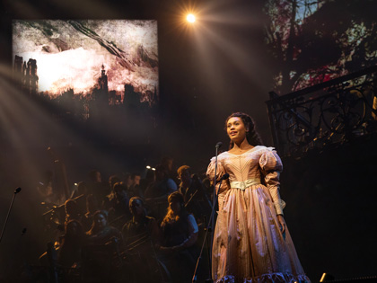 A young girl wearing a thick pink dress, singing on stage. 