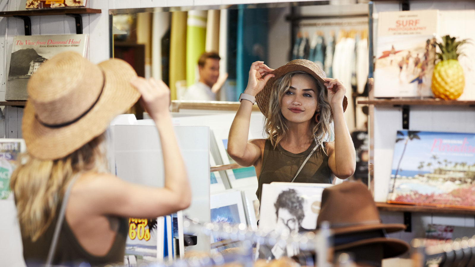 Woman trying on a hat and looking in a mirror.